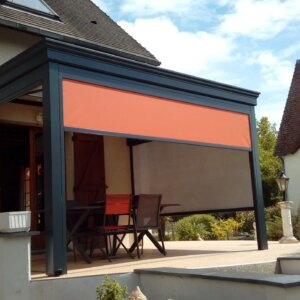 Pergola Gris Anthracite avec stores oranges sur terrasse en béton surélevé